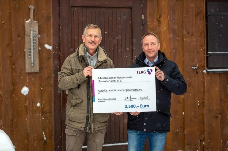 Vor der Jahnhütte des Schmalkaldener Wandervereins "Turnvater Jahn" e. V. stehen Vereinsvorsitzender Helmut Wicke und der Geschäftsführer der Netzgesellschaft Schmalkalden, Knut Weißenborn, mit einem Spendenscheck über 2500 Euro.